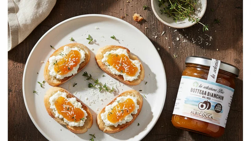 Vier Häppchen mit Frischkäse und Aprikosen-Konfitüre von Bottega Bianchin auf weißem Teller, Thymian und das Glas daneben